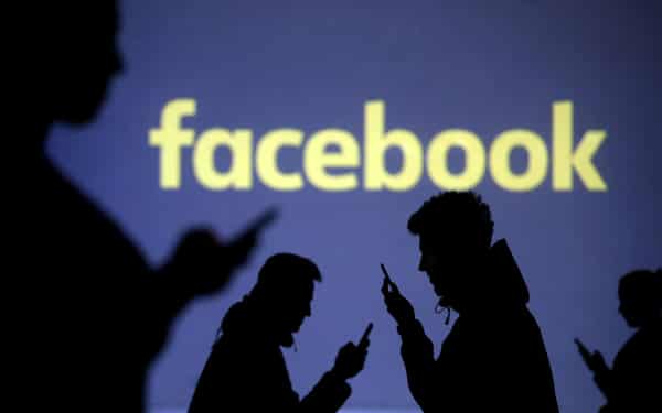 FILE PHOTO: Silhouettes of mobile users are seen next to a screen projection of Facebook logo in this picture illustration