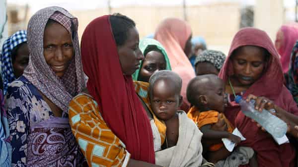 Women wait with their children under a shed for food rations at a internally displaced persons (IDP) camp on the outskirts of Maiduguri, northeast Nigeria