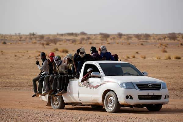 Migrants crossing the Sahara desert into Libya ride on the back of a pickup truck outside Agadez