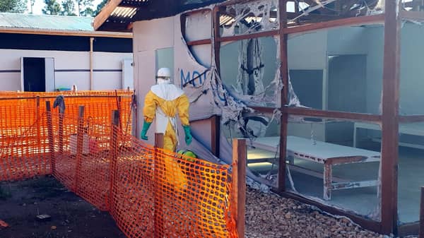 A health worker dressed in a protective suit walks past burned structures after attackers set fire to an Ebola treatment center run by Medecins Sans Frontieres (MSF) in the east Congolese town of Katwa