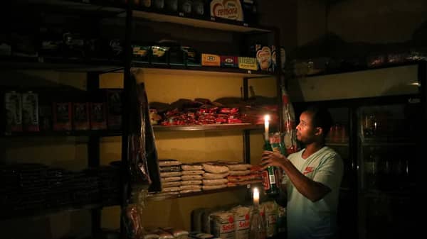 FILE PHOTO: Mulugeta Desalegn, an owner of a convenience store, or “spaza shop”, picks an item for a customer as he holds a candle, in Senaone