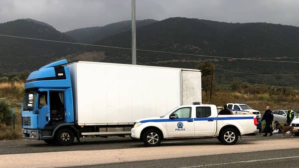 Police officers stand next to a refrigerated truck carrying migrants, after a check at a motorway near Xanthi