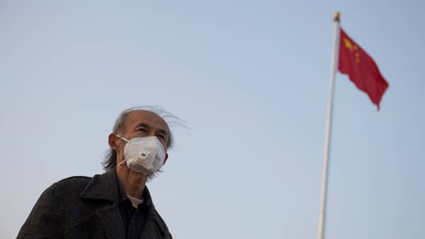 Man wearing a mask looks on near a Chinese national flag at the Tiananmen Square, as the country is hit by an epidemic of the new coronavirus, in Beijing