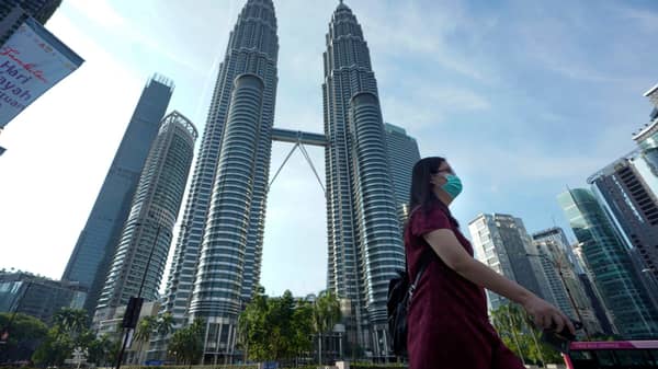 A woman wearing a face mask walks in front of Twin Towers in Kuala Lumpur, Malaysia, Wednesday, March 18, 2020 (AP Photo/Vincent Thian)