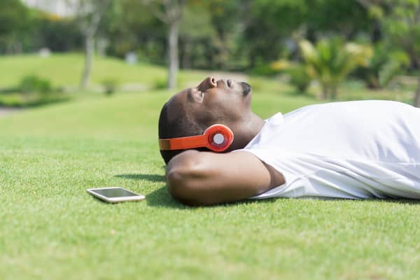 Serene black man resting in park and listening to music