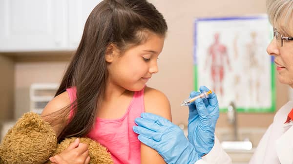 Female doctor and latin descent girl patient in pediatrician’s office or clinic getting vaccination.