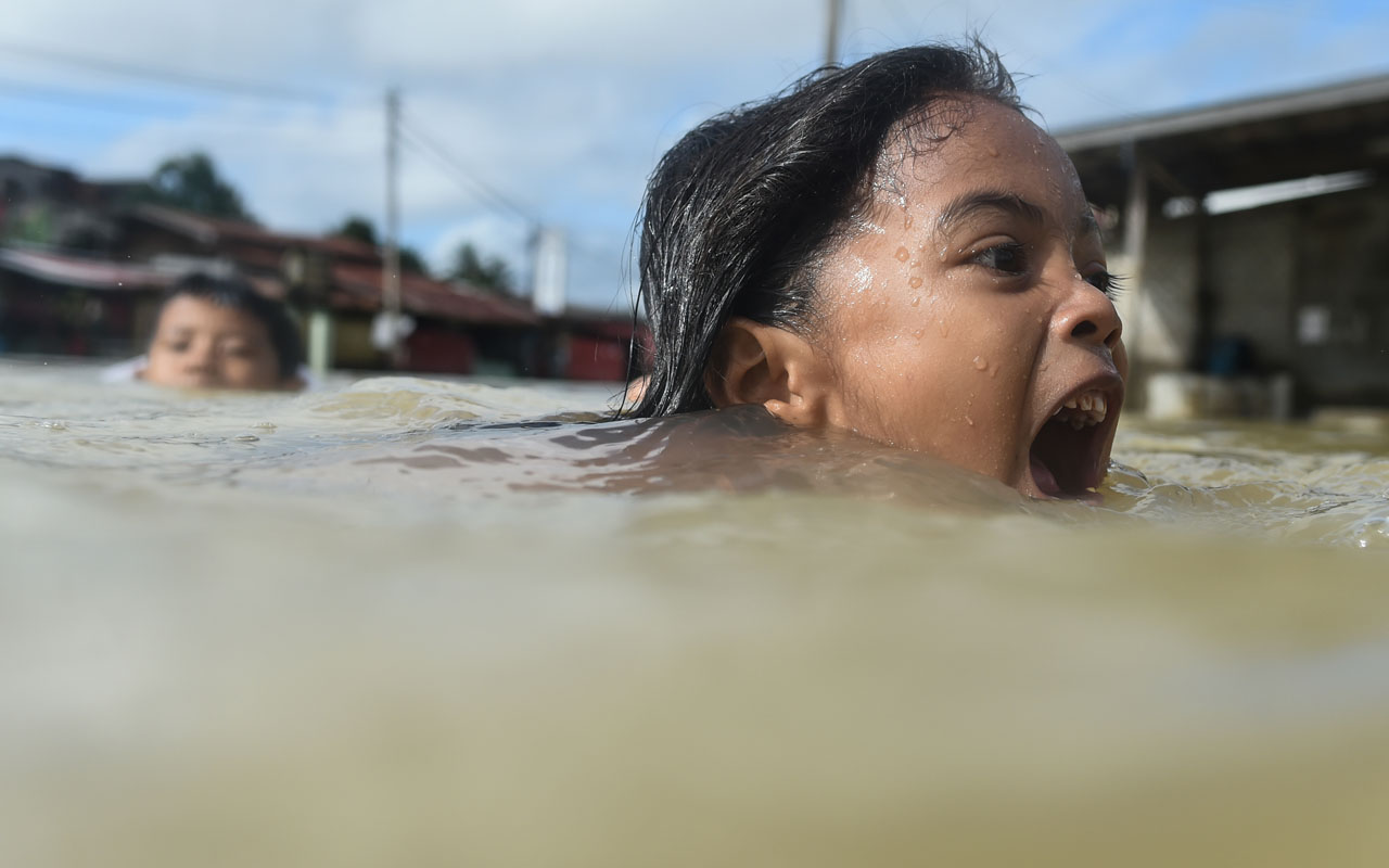 Children swim in floodwaters in Malaysia's northeastern town of Rantau Panjang, which borders Thailand, on January 5, 2017. Floods in two northeast Malaysian states have now forced almost 23,000 people from their homes and extra relief centres have been opened, rescue officials said January 4. / AFP PHOTO / Mohd RASFAN