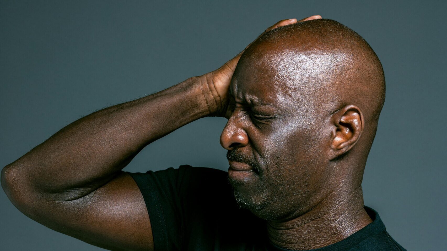 A man on black polo with hands touching his head