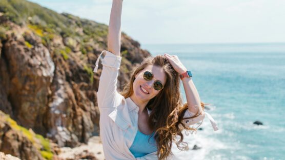 Woman out in the sun holding a hat and wearing sunglasses