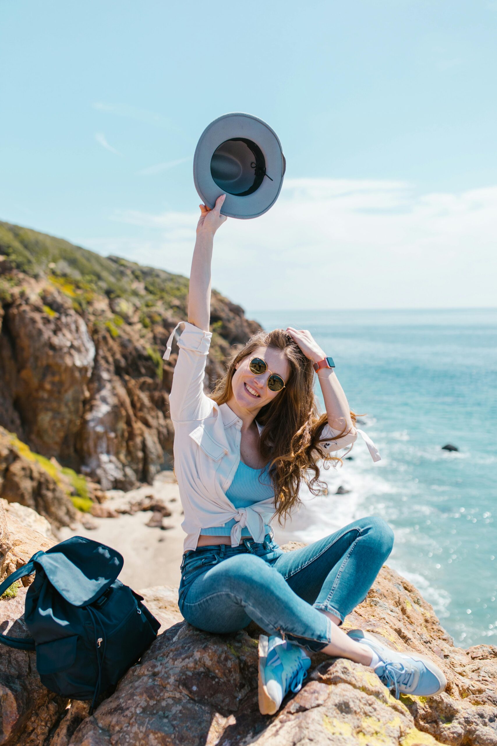 Woman out in the sun holding a hat and wearing sunglasses