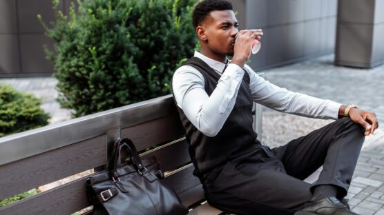 A man seating and taking a drink with bag by the side